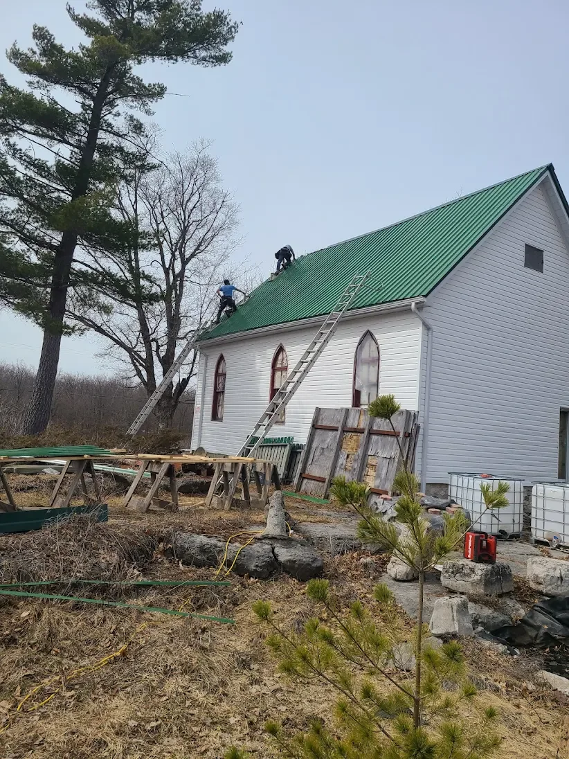 White building with green metal roofing being installed.