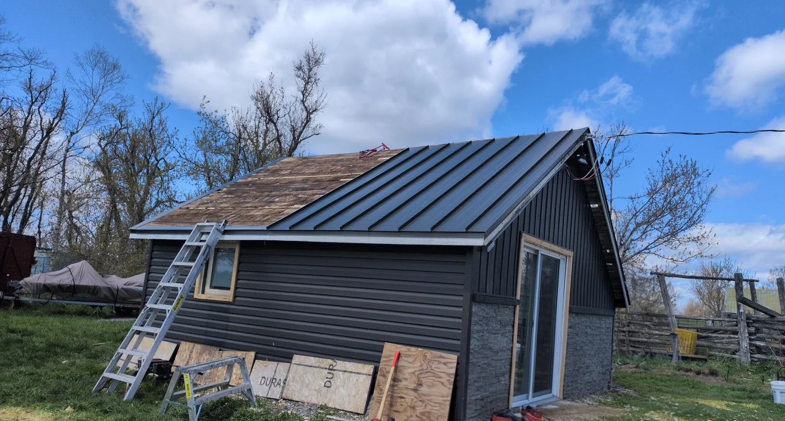 Black standing seam panels being installed on a gray house roof.