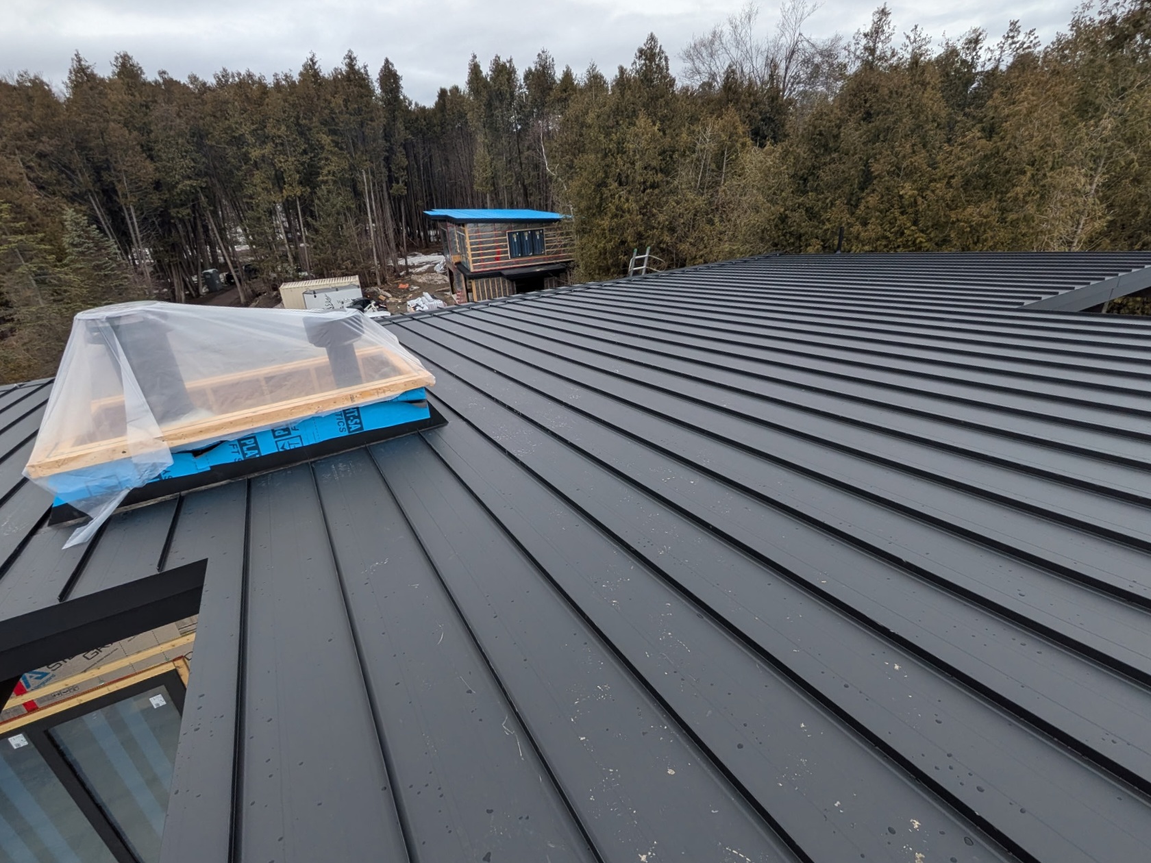 Close view of dark standing seam panels around a skylight curb.