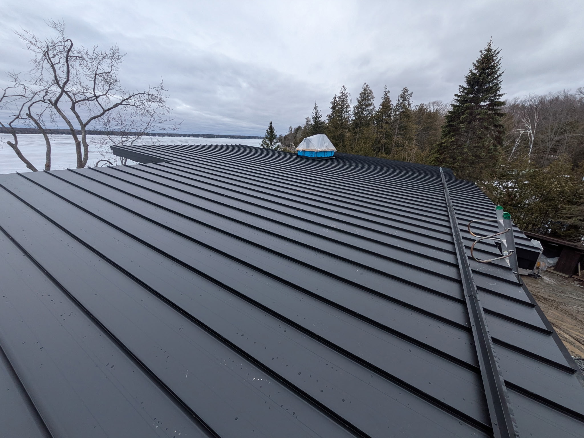 Wide lakefront view across a standing seam roof with a frozen lake beyond.
